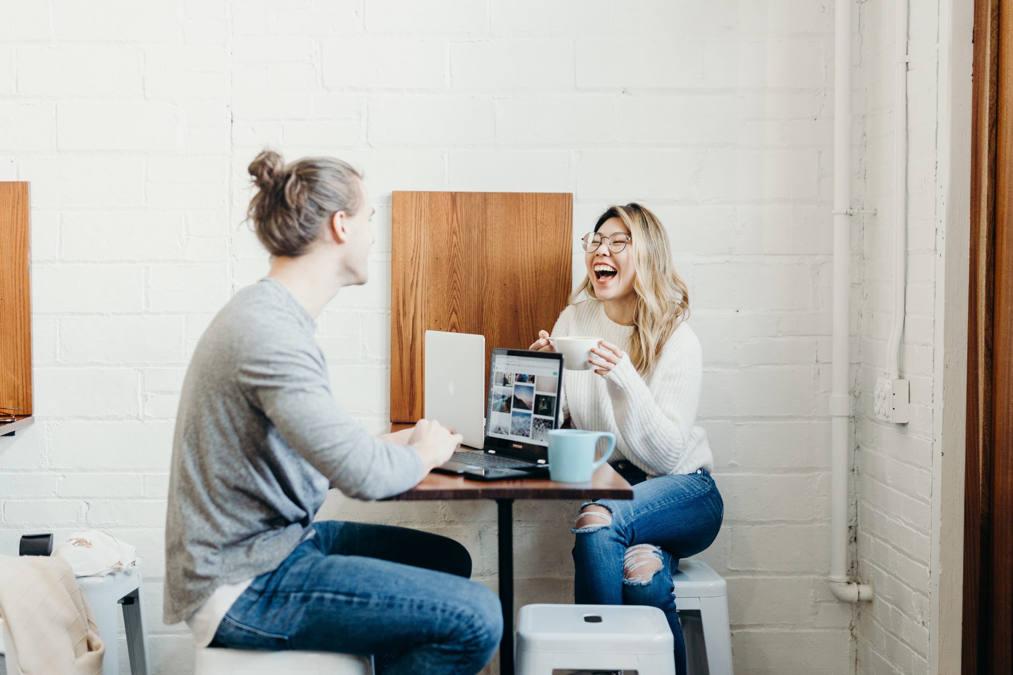 different personality types man and woman laughing while working at a cafe on laptops